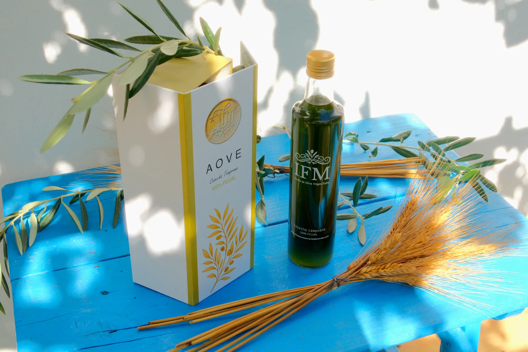 The IFM gift box and bottle on the blue table, with an olive branch.